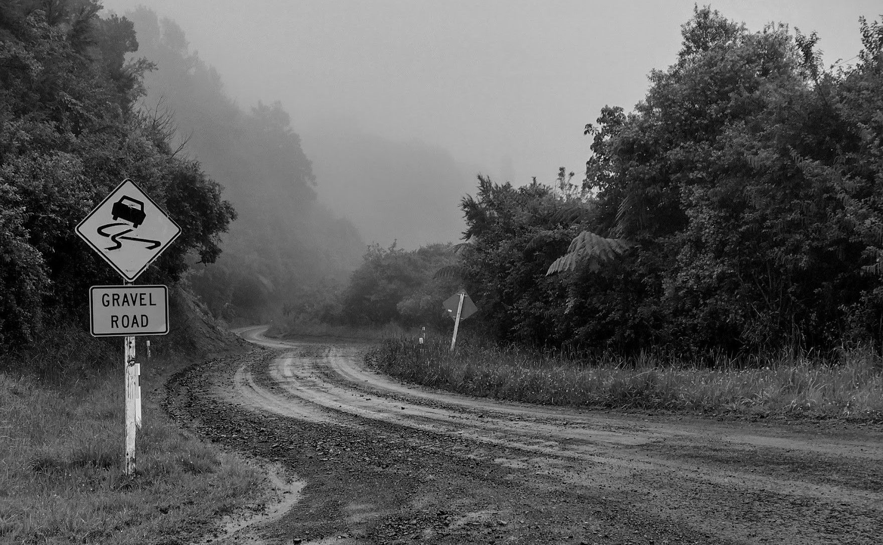 A gravel road curls into the mist. A sign warns that the road is dangerous